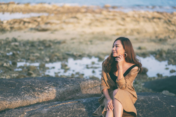 A beautiful asian woman enjoy sitting on the rock by the seashore - Fotografie, Obrázek