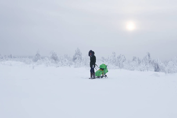 Perm Krai, Russia - January 02, 2021: woman with baby carriage walks in winter snowy area on frosty day - Foto, Imagen