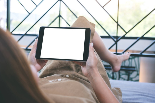 Mockup image of a woman holding black tablet pc with blank white desktop screen  while laying down in living room with feeling relaxed - 写真・画像