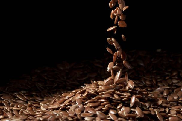 Close up of linseeds or flax seed on dark background with some falling in a narrow stream spread in the middle of the frame - Photo, image