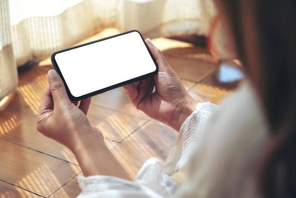 Immagine mockup di una donna che tiene e utilizza il telefono cellulare nero con schermo desktop vuoto orizzontalmente mentre si sdraia sul pavimento con sensazione di rilassamento - Foto, immagini
