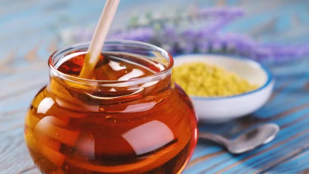 Med ve skleněném hrnci s medovým rozparovačem přes modré dřevěné pozadí - Záběry, video