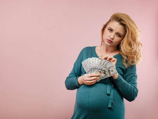 Egy terhes nő számolja a pénzt. Egy terhes nő portréja zöld ruhában velünk dollárban. - Fotó, kép