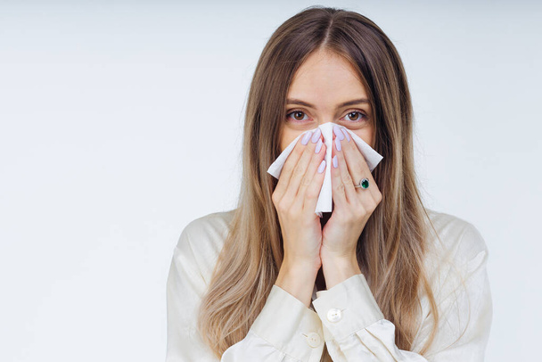 Ein junges krankes Mädchen im weißen Hemd niest, hält ein Taschentuch in der Hand und wischt sich die laufende Nase ab. Studentin hat saisonale Allergie oder chronische Sinusitis - Foto, Bild