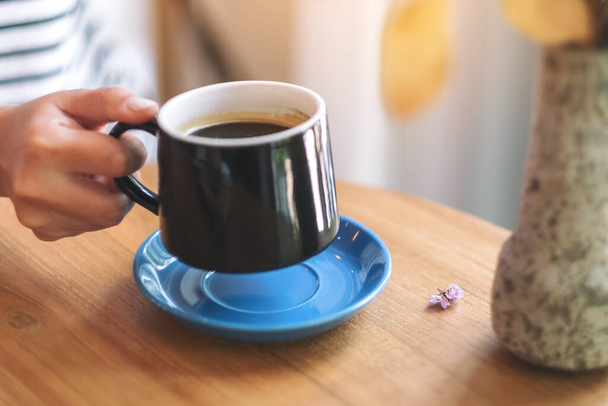 Closeup image of a woman's hand holding a green cup of hot coffee on wooden table - Photo, Image