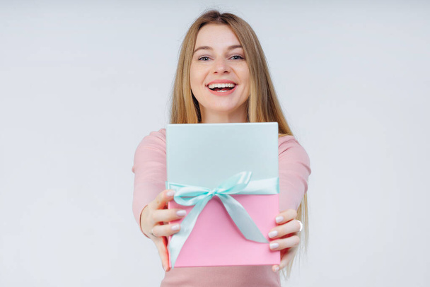 Smiling cheerful girl makes a surprise, presents gift box with ribbon bow. - 写真・画像