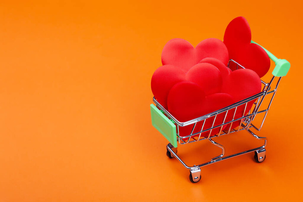 Many red hearts inside mini grocery cart on colored background - Photo, Image
