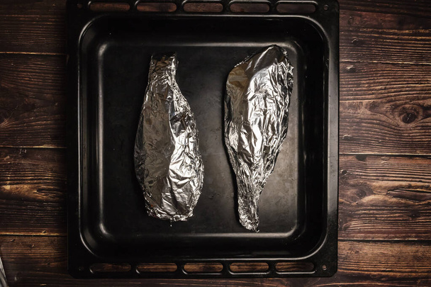 Peixe embrulhado em papel alumínio em uma assadeira e em uma mesa de madeira. Cozinhar peixe no forno - Foto, Imagem