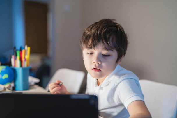 Ödevi için tablet kullanan yeni normal bir çocuk, dijital tablet araması kullanarak ev ödevi yapan çocuk internet, e-öğrenim, evde eğitim kavramı hakkında bilgi topluyor. - Fotoğraf, Görsel
