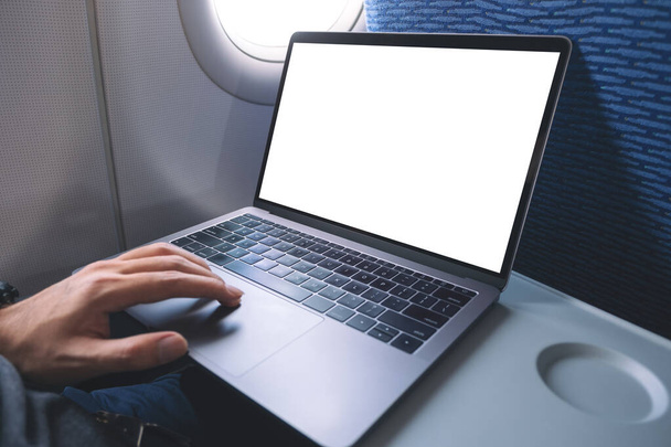 Mockup image of a man using and touching on laptop computer touchpad with blank white desktop screen while sitting in the cabin - Foto, Bild