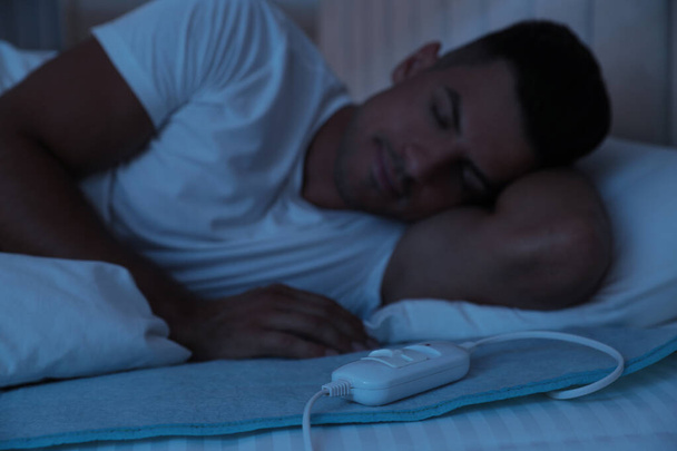 Homem dormindo na cama com almofada de aquecimento elétrico, foco no cabo - Foto, Imagem