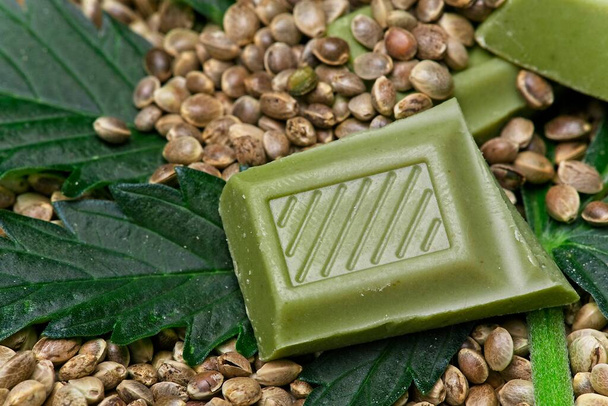 Шматочки зеленого шоколаду канабісу лежать на листі канабісу та їстівному насінні
. - Фото, зображення