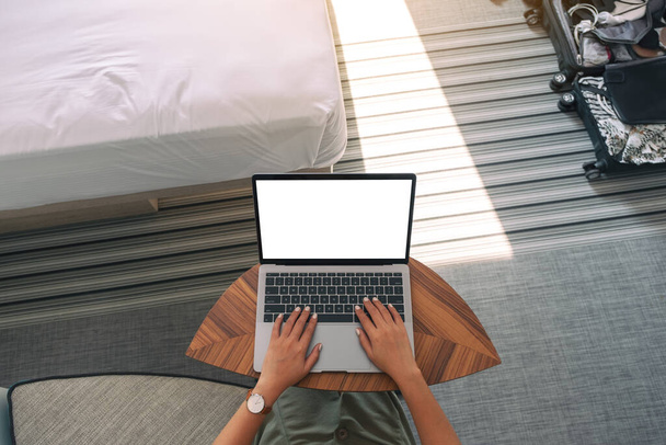 Top view mockup image of a woman using and typing on laptop with blank white desktop screen keyboard on wooden table next to the bed - Zdjęcie, obraz