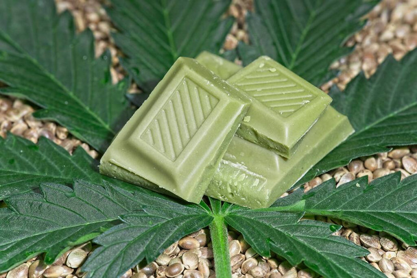 Cijfers van groene cannabis chocolade liggend op cannabisblad en eetbare zaden. - Foto, afbeelding