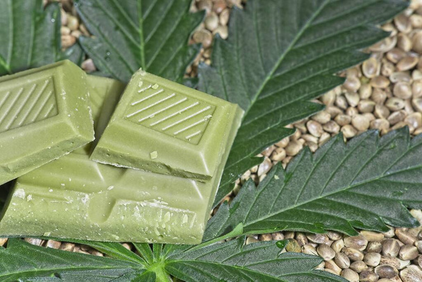 Des morceaux de chocolat vert de cannabis couchés sur des feuilles de cannabis et des graines comestibles. - Photo, image