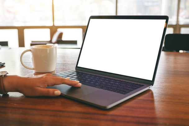Образец женской руки с помощью тачпада для ноутбука с чистым белым экраном рабочего стола с чашкой кофе на деревянном столе  - Фото, изображение