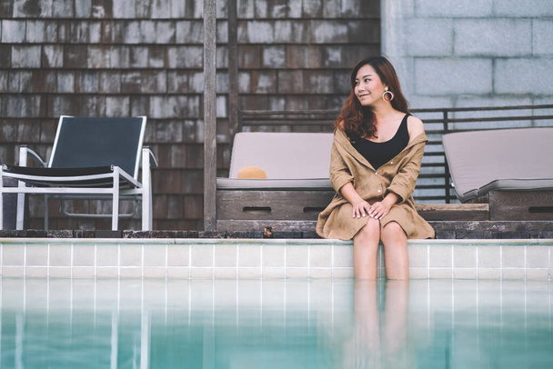 Portrait image of a beautiful asian woman enjoyed sitting by the swimming pool - Фото, изображение