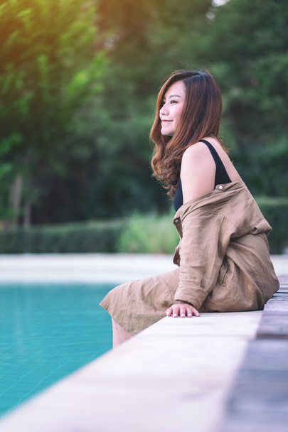 Portrait image of a beautiful asian woman enjoyed sitting by the swimming pool - Photo, Image