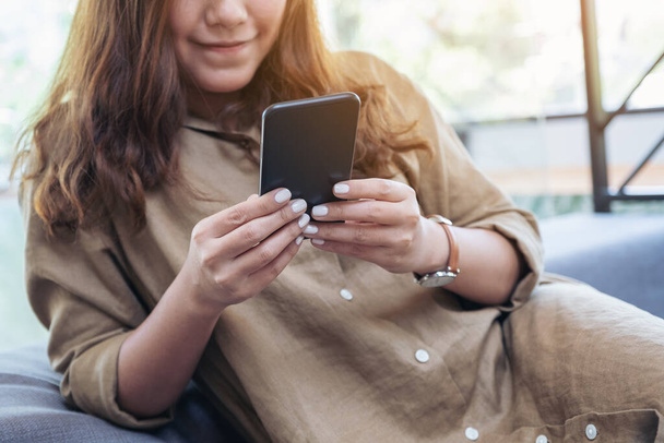 Detailní obrázek krásné asijské ženy drží, používá a dívá se na chytrý telefon, zatímco sedí v obývacím pokoji - Fotografie, Obrázek