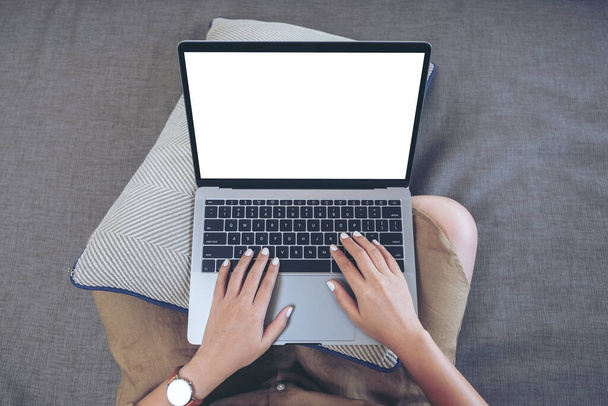 Top view mockup kép egy nő használ és gépel a laptop billentyűzetén üres fehér képernyő, miközben ül a nappaliban - Fotó, kép