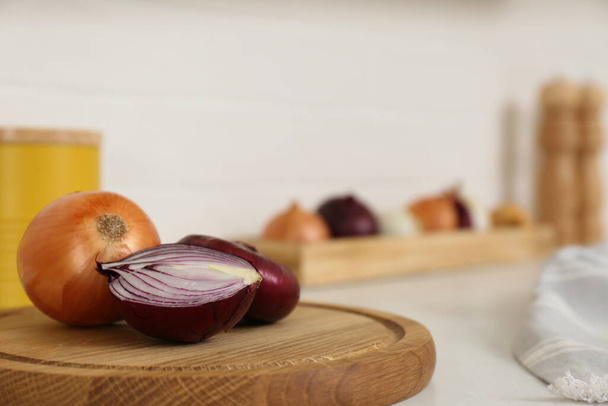 Fresh cut and whole onions on wooden board in modern kitchen, closeup. Space for text - Foto, afbeelding