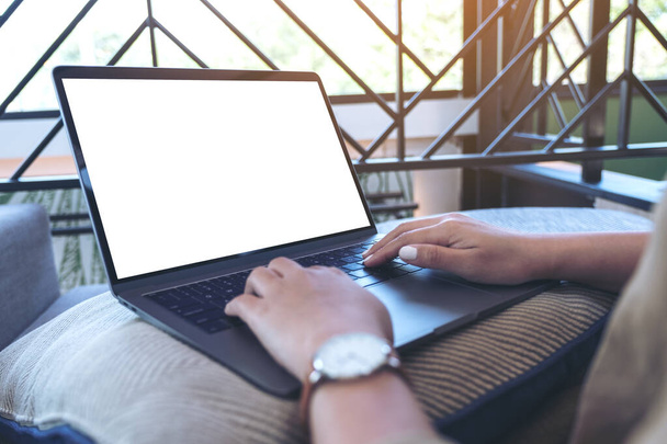 Εικόνα mockup μιας γυναίκας που χρησιμοποιεί και πληκτρολογεί σε πληκτρολόγιο laptop με λευκή οθόνη ενώ κάθεται στο σαλόνι - Φωτογραφία, εικόνα
