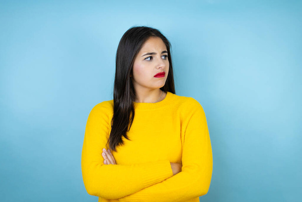 Young beautiful woman wearing yellow sweater over isolated blue background thinking looking tired and bored with crossed arms - Φωτογραφία, εικόνα