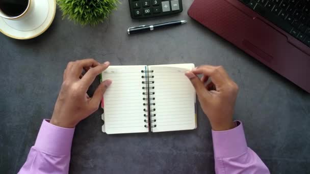 Draufsicht der Hand beim Drehen eines Notizblocks mit Laptop auf dem Tisch  - Filmmaterial, Video