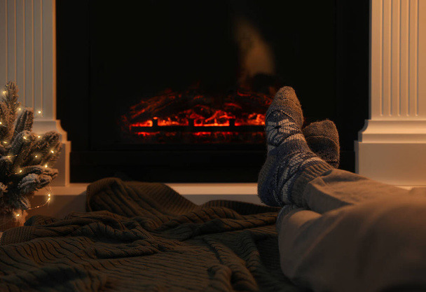 Man in warm socks resting near fireplace at home, closeup. Space for text - Φωτογραφία, εικόνα