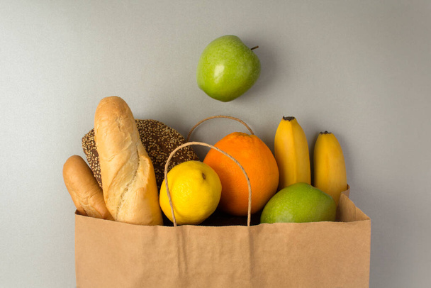 Papiertüte mit Früchten und Brot auf der grauen Oberfläche - Foto, Bild