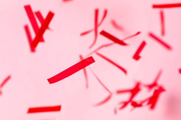 Glanzende rode confetti vallen neer op roze achtergrond - Foto, afbeelding