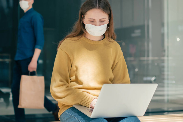 young woman in a protective mask using a laptop near a shopping center. - Fotoğraf, Görsel