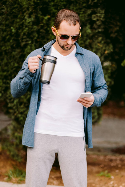 Muž v bílém tričku s telefonem a nápojem na kávu - Fotografie, Obrázek