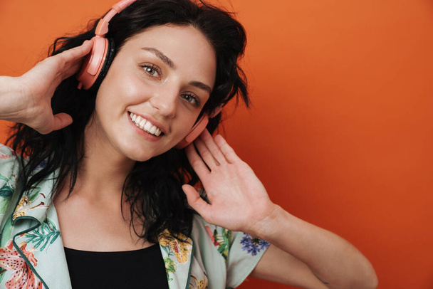 Photo of young positive happy woman listening music by headphones isolated over orange wall background - Valokuva, kuva