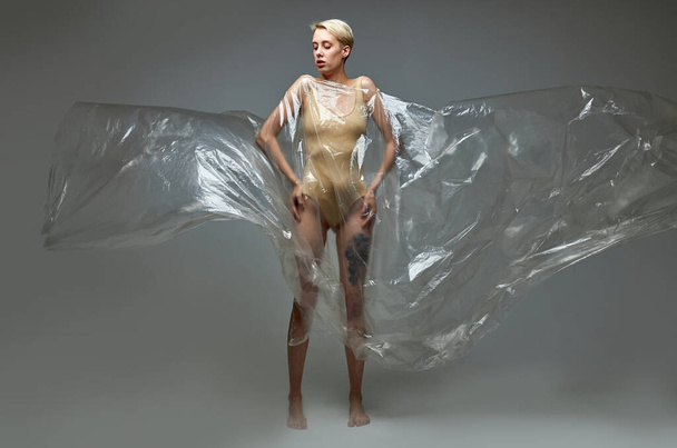portrait of slender caucasian female in bodysuit posing in polyethylene bag - Foto, Imagem