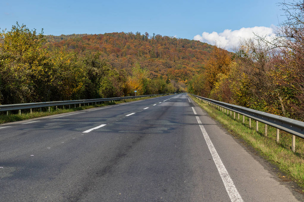 Herfst berglandschap - vergeelde en rode herfstbomen in combinatie met groene naalden en blauwe lucht aan de kant van een verlaten weg. Kleurrijke herfst landschap scène in de Oekraïense Karpaten. - Foto, afbeelding