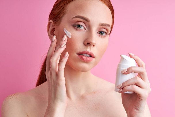 shirtless caucasian woman applying face cream isolated over pink wall - Foto, immagini