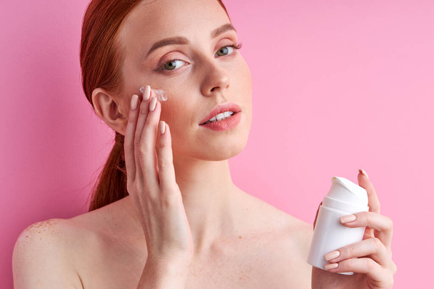 beautiful caucasian redhead woman is applying moisturizer for smooth skin - Foto, imagen