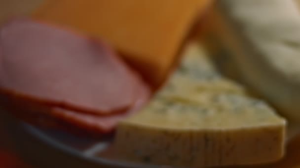 Vari tipi di formaggi salati e freschi e prosciutto di maiale pronto per essere tagliato come antipasto, video 4K. Scatto artistico, rallentamento - Filmati, video