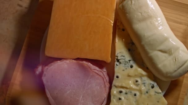 Vari tipi di formaggi salati e freschi e prosciutto di maiale pronto per essere tagliato come antipasto, video 4K. Rallentamento, vista dall'alto - Filmati, video