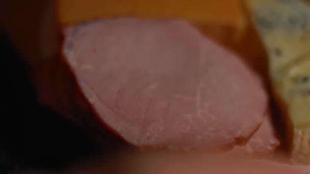 Vari tipi di formaggi salati e freschi e prosciutto di maiale pronti per essere tagliati come antipasto e disposti su un vassoio di legno. Video 4K. Scatto artistico, rallentamento - Filmati, video