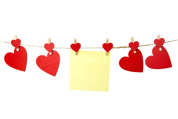 Κενό κίτρινο κολλώδες σημείωμα κρέμονται με κόκκινες καρδιές απομονώνονται σε λευκό φόντο, ρομαντική έννοια Ημέρα του Αγίου Βαλεντίνου, αντίγραφο χώρου. Χώρος για κείμενο - Φωτογραφία, εικόνα