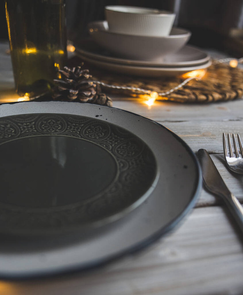 czarno-białe talerze z dekoracjami świątecznymi na białym drewnianym stole ze światłami  - Zdjęcie, obraz