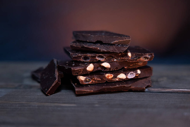 Pieces of chocolate on a wooden table on a brown background and orange lights - Photo, Image