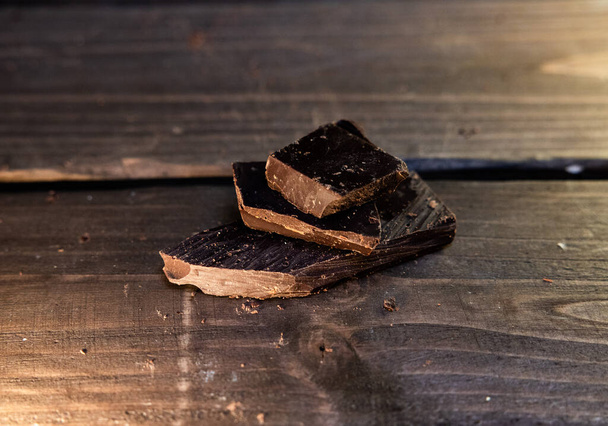 Pieces of chocolate on a wooden table on a brown background  - Photo, Image
