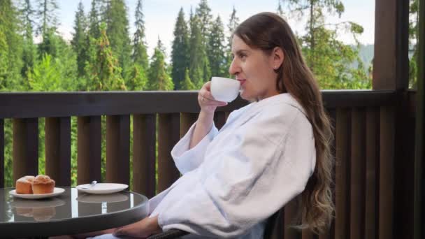 Hymyilevä nainen juo teetä ja katselee vuorta hotellihuoneestaan. Käsite ihmiset matkustavat, matkailu ja loma vuorilla kesällä - Materiaali, video