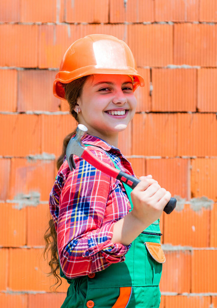 Repair concept. kid wear helmet on construction site. teen girl builder with building tool hammer. child on repairing work. concept of renovation in workshop. busy professional carpenter - Foto, Imagen