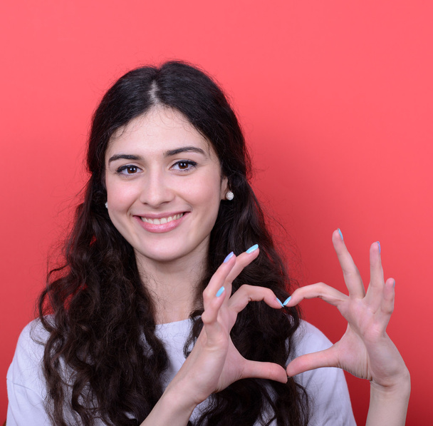 Portrait of happy woman making heart shape with hands against re - Φωτογραφία, εικόνα