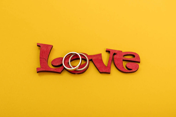 Svatební prsteny s dřevěným slovem láska na žlutém pozadí. Valentýnská koncepce. - Fotografie, Obrázek