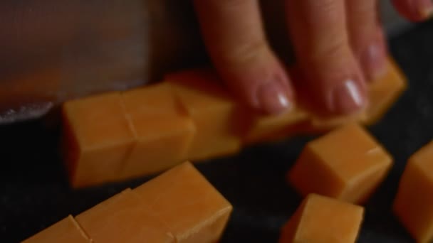 Çedar peyniri bloğu kesme tahtasıyla kesiliyor. Lezzetli aperatif olarak küp çedar peyniri. 4K video - Video, Çekim